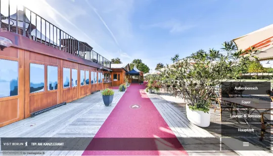 Roter Teppich auf einer sonnigen Restaurantterrasse mit Pflanzen und Holzwänden.