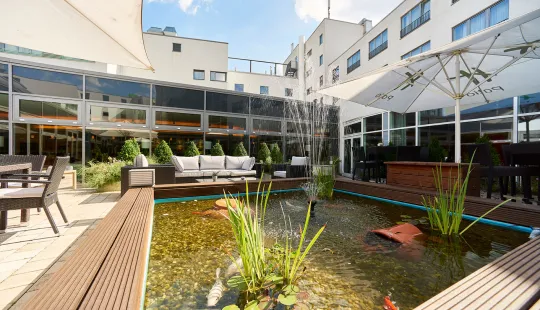 Innenhof mit Teich, Sitzgelegenheiten und Sonnenschirmen an einem modernen Gebäude