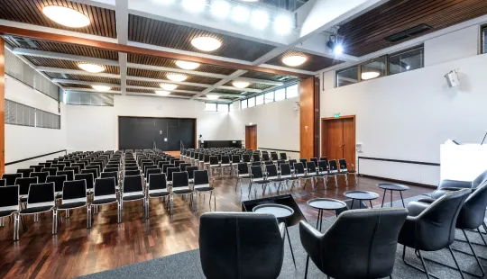 Leerer Konferenzraum mit Stuhlreihen, Podium und moderner Beleuchtung.