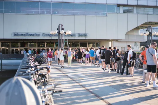 Crowd gathers in front of the entrance of the International Congress Center Berlin on a sunny day