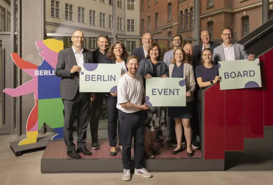 Gründer:innen des Berlin Event Board stehen auf eine Treppe und halten Schilder mit den Wörtern Berlin, Event und Board hoch