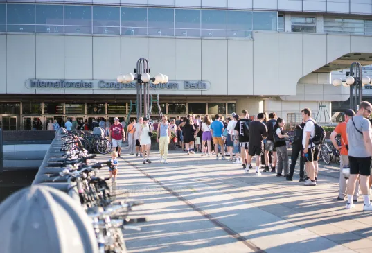 Crowd gathers in front of the entrance of the International Congress Center Berlin on a sunny day
