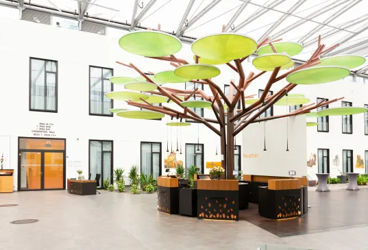 Modern lobby with large tree sculpture and round green canopy leaves, surrounded by desks.