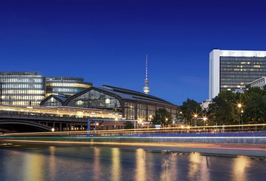 Cityscape with modern buildings, a bridge, and a river at dusk under a clear sky.