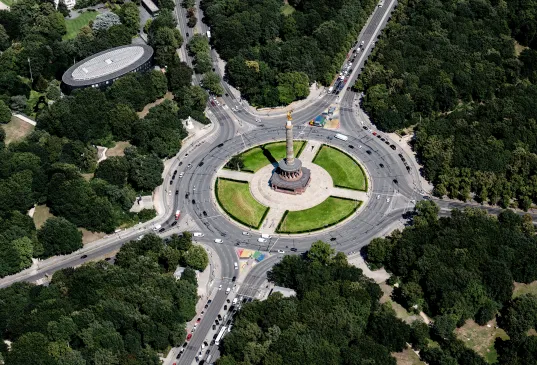 Aerial view of a circular monument surrounded by roads and dense green trees.