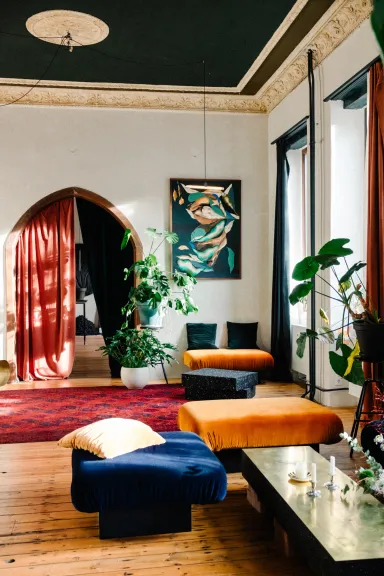 Helles Wohnzimmer mit bunten Sitzkissen, Pflanzen und großen Fenstern