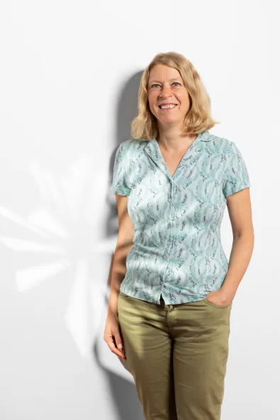 Photo of a smiling woman wearing a blue top and green pants, Leonie Umbach, Project Manager for Sustainable Berlin at the Berlin Convention Office