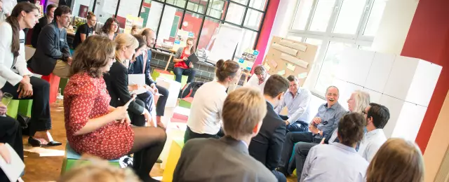 Meet and Change Infoveranstaltung, Teilnehmende sitzen auf bunten Hockern im Sitzkreis vor Pinnwand