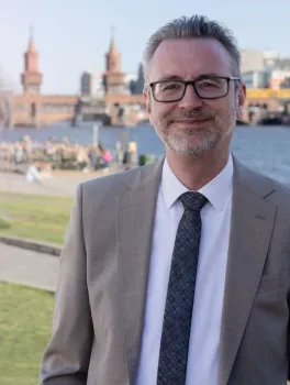 Geschäftsführer, Dr. Jürgen Amann im Anzug vor Spee und Stadtlandschaft mit Brücke im Hintergrund