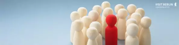 Holzfiguren die einen Kreis bilden, in der Mitte steht eine rote im Zentrum