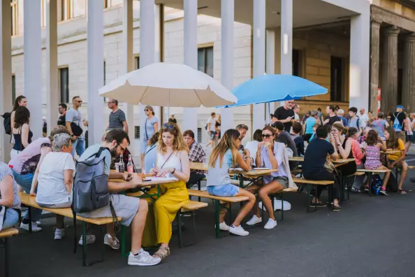 Foto: Menschen sitzen im Sommer auf Bierzeltgarnituren vor dem Bodemuseum, Essen von Foodtrucks
