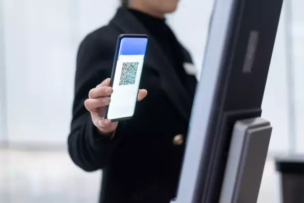 Eine Person hält ein Smartphone mit einem gut lesbaren QR-Code vor ein digitales Check-in-Terminal.