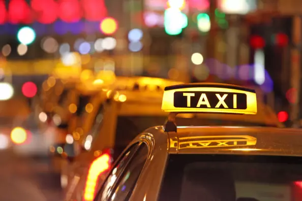 Illuminated taxi sign and city traffic, cars waiting in line