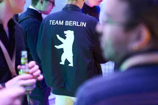 Person wearing a "TEAM BERLIN" jacket with a white bear graphic at a social gathering.