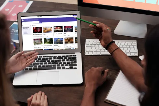 Zwei Personen besprechen gemeinsam Inhalte auf einem Laptop-Bildschirm am Schreibtisch.