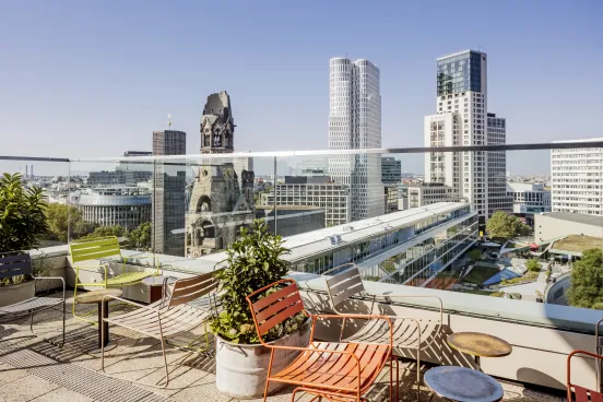 Rooftop terrace with colorful chairs overlooking the Berlin cityscape with modern and historic buildings.