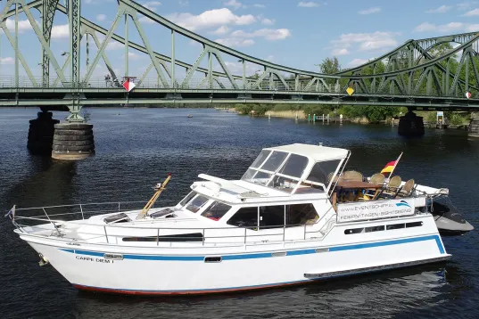 White motorboat on river near a green metal bridge on a sunny day.