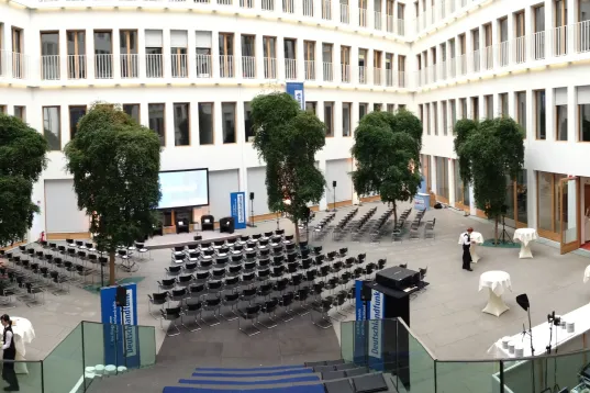 Orderly inner courtyard with rows of chairs, trees and a stage, set up and ready for an event.