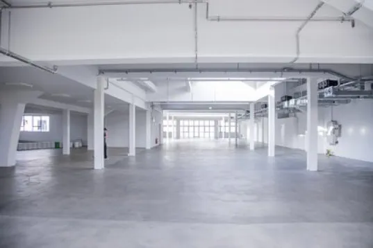 Spacious empty warehouse with white walls and large windows.