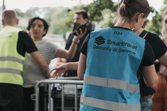 Security staff in blue vests managing a line of people outdoors.