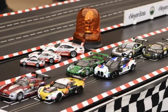 Slot cars lined up at the start of a miniature racetrack with a checkered flag.