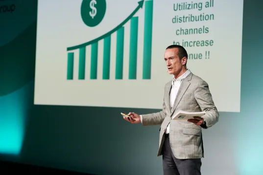 Man in a grey blazer presenting beside a rising bar chart with a dollar sign.