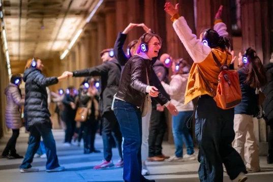 Participants wearing illuminated wireless headphones dance and interact during a Silent Disco Tour in Berlin’s urban outdoor setting at night.