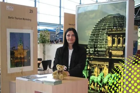 Frau am Infostand mit Teddy, im Hintergrund ein Foto des Berliner Reichstags.