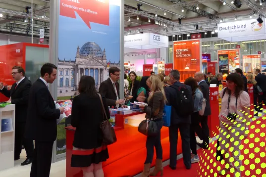 Menschen unterhalten sich an einem roten Messestand auf einer Messe.