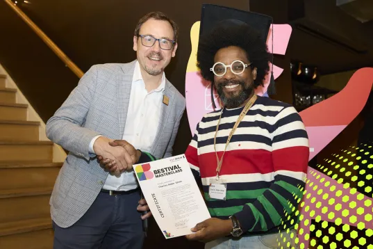 Zwei Männer lächeln und geben sich die Hand, einer hält ein Zertifikat.