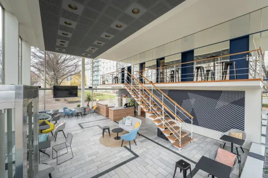 Modern lounge with tables, chairs, large windows, and a staircase leading to an upper level.
