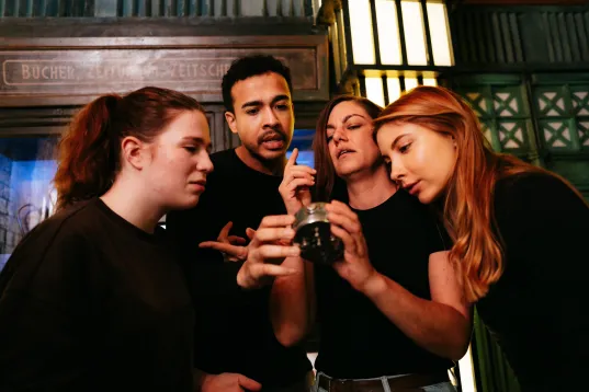 Four people closely examining a small jar together indoors.