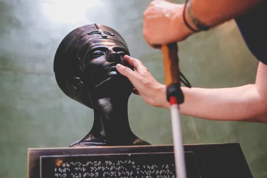 A woman touches a sculpture in the exhibition “In the Light of Amarna”