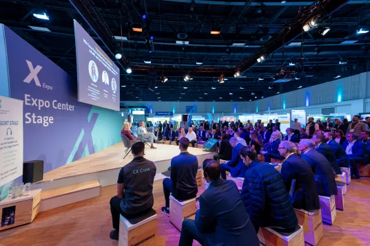 Participants sit in front of a small stage marked as the Expo Stage.