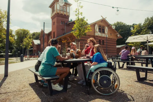 A group of young people in the beer garden at the Eierhäuschen, including one person in a wheelchair, on a sunny day