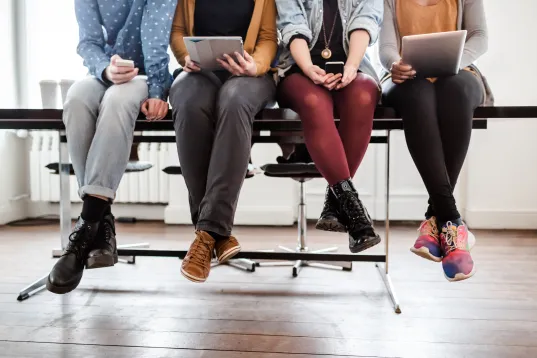 our people sit side by side on a table edge holding tablets or smartphones.