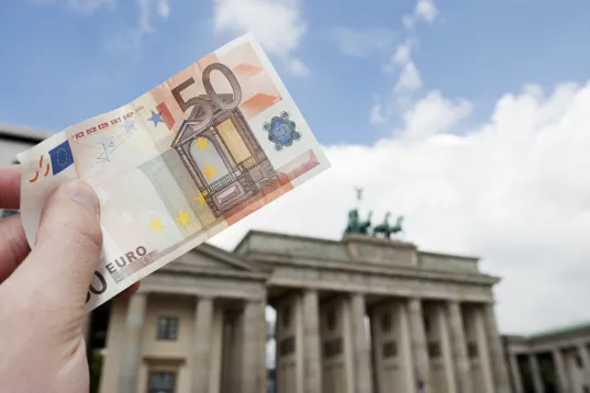 Vor dem Brandenburger Tor wird ein 50-Euro-Schein von einer Hand in die Luft gehalten