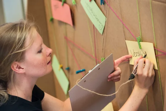 A woman is writing on a MEET & CHANGE card hanging on the wall.