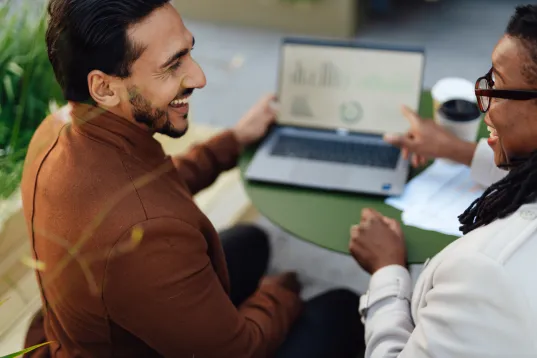 Zwei Personen im Gespräch, eine zeigt auf Diagramme auf einem Laptopbildschirm