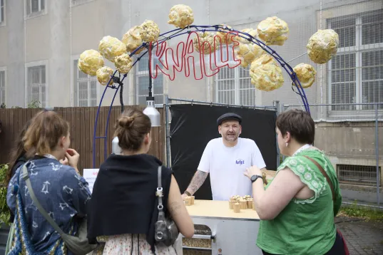 A popcorn stand with three people standing around listening to the stallholder.