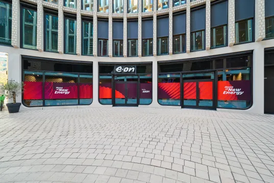 Moderne Glasfassade mit rotem Banner und weißem Logo in einem Innenhof.