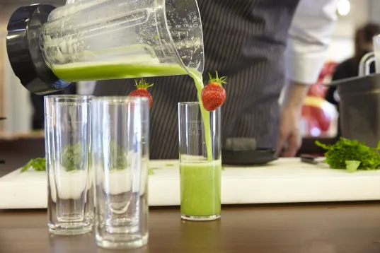 The image shows green juice being poured from a blender into a glass