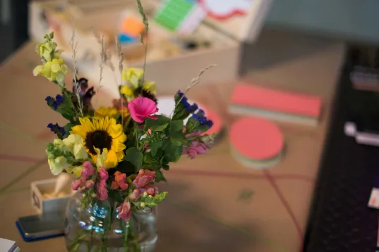 German→British English Translator sagte:  MEET & CHANGE desk with colourful documents, a small bouquet of flowers and office accessories.