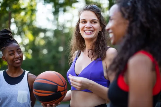 Group of multi-ethnic women with a basket ball on outdoors court. Females in sports wear talking after a game of basketball.