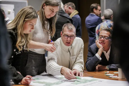 People gathered around a table discussing and pointing at a large map or plan.