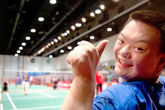 A boy at the Special Olympic World Games 2023 is shown giving a thumbs up and smiling with jo