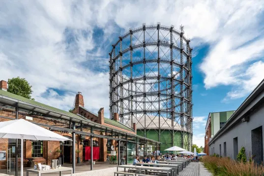 iew of the EUREF Campus in Berlin with the Gasometer, terraces, and modern architecture under a blue sky.