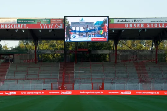 Leeres Fußballstadion mit grüner Spielfläche und überdachter Tribüne, Aufnahme bei Tageslicht
