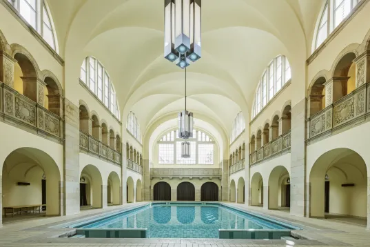 Indoor swimming pool with arched windows and ornate balcony railings.