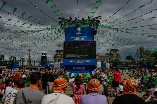 Menschenmenge schaut bei bewölktem Himmel auf große Leinwand bei Public Viewing.